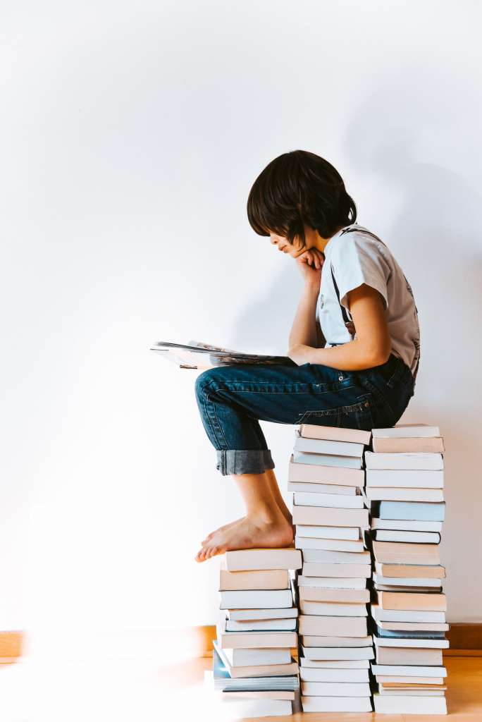 dziecko siedzi na książkach i czyta książkę