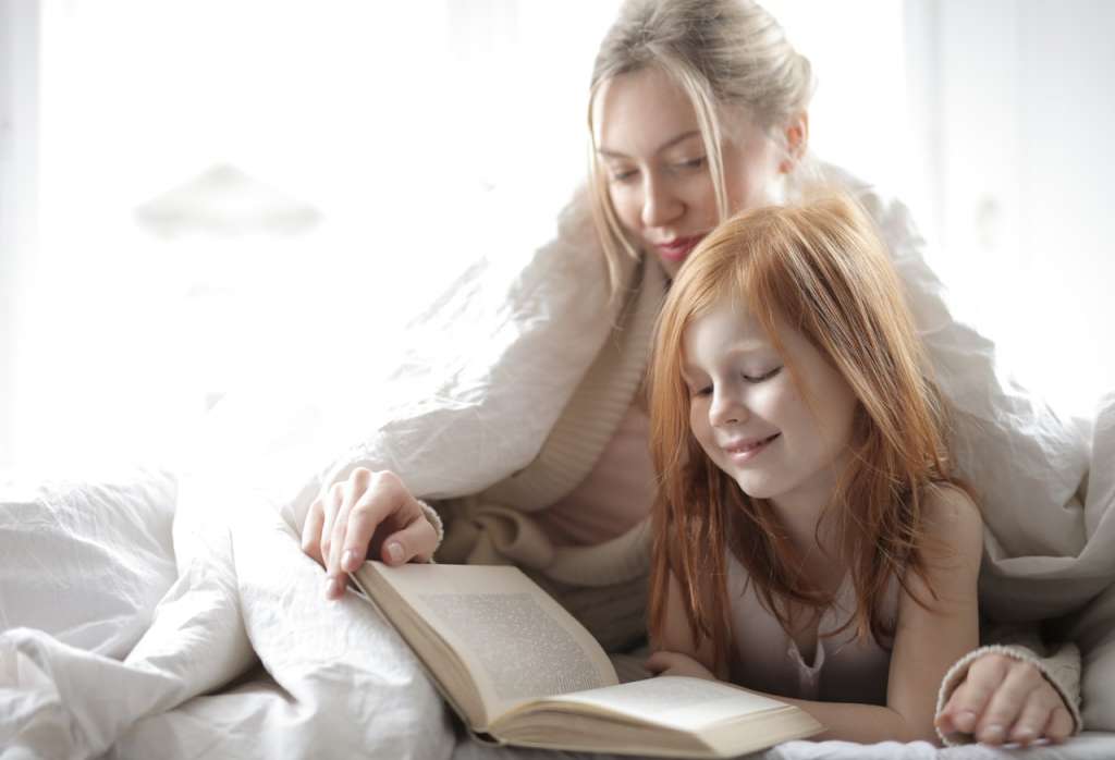 matka z dzieckiem czytają książkę w łóżku